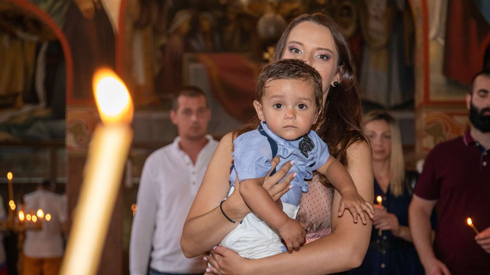 Запалена свещ и кръстница с бебето по време на ритуала
