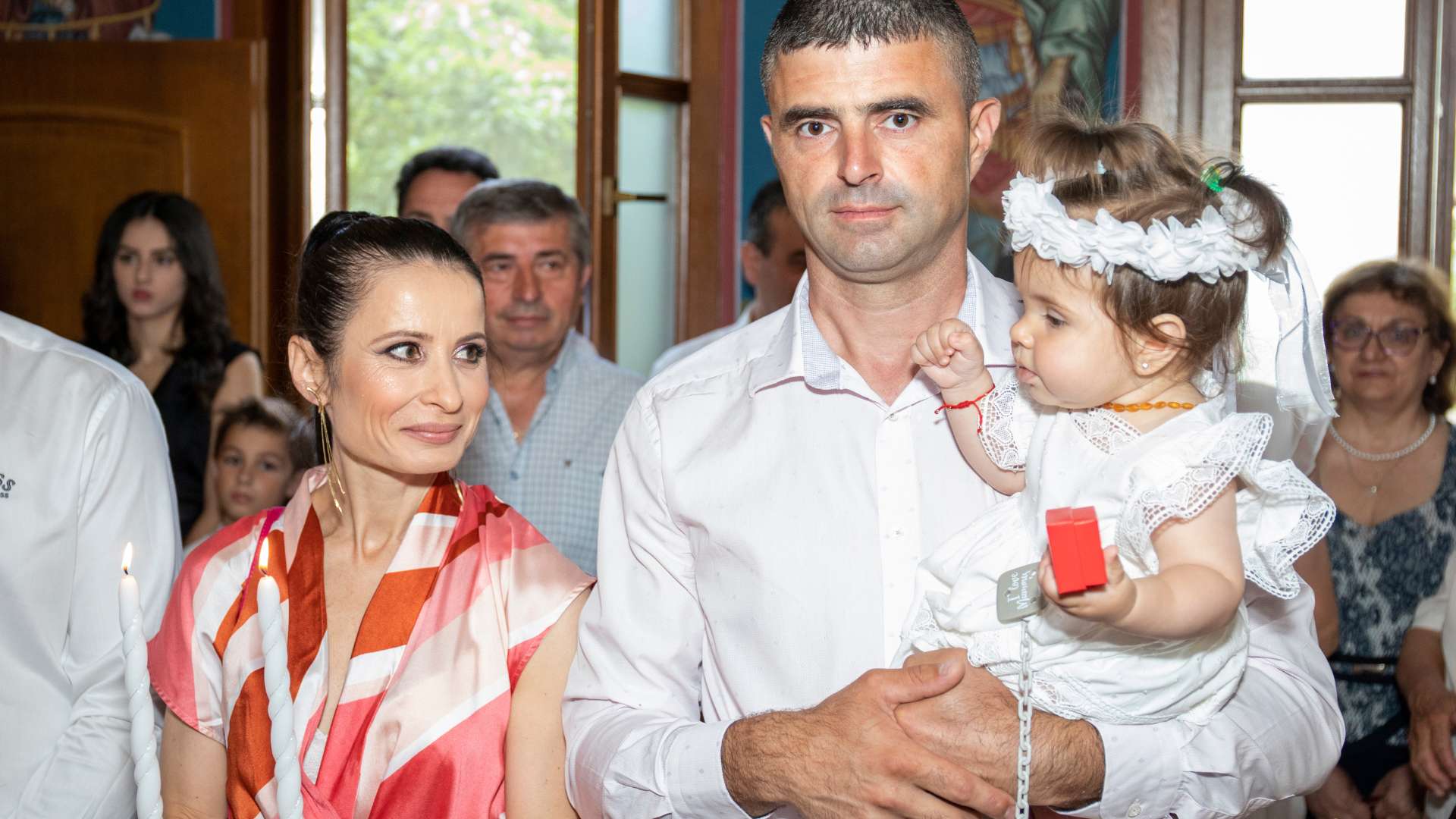 Родители с дъщеря си в бяла рокля след кръщенето